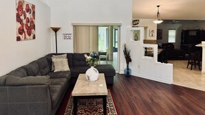 Un salon moderne avec un canapé d’angle gris foncé, une table basse agrémentée d’un vase et un coin repas avec un bar.