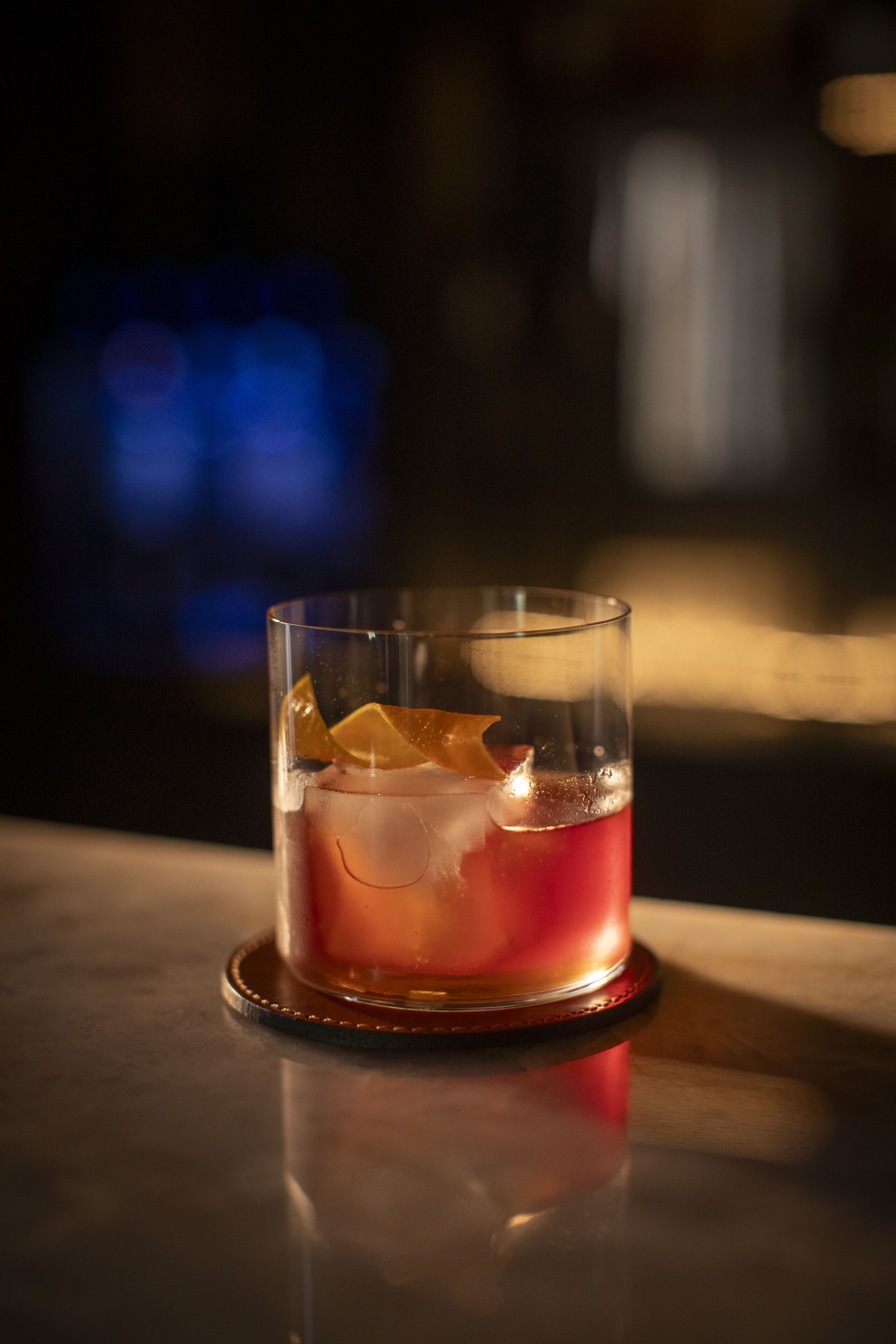 A glass of red beverage with ice cubes on a coaster.