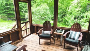 Une terrasse en bois avec des chaises Adirondack et une table, donnant sur une zone boisée.