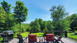 Une terrasse dotée de mobilier d’extérieur, d’un barbecue et offrant une vue sur une zone boisée.
