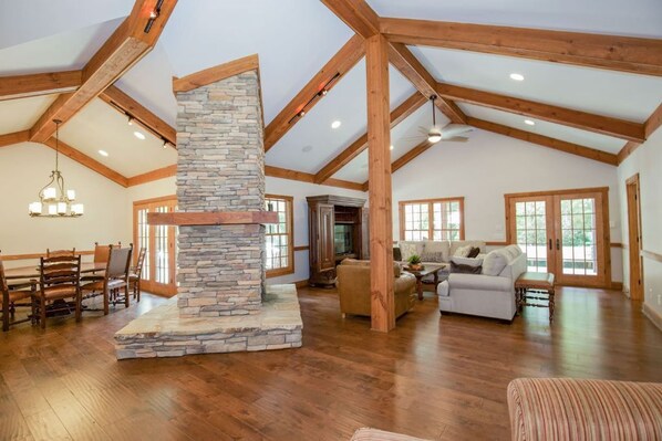 A spacious living area with a stone fireplace, wooden beams, and a dining area with a wooden table and chairs. - Pinehurst Golf home w/ pool,Game room, Pool table, sleep up to 12 (Pinehurst)