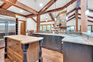 A spacious kitchen with a large island, wooden beams, and a stone fireplace.