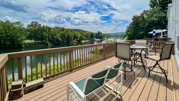 A deck with outdoor furniture overlooking a river and greenery. - Lake Taneycomo Waterfront Condo | Marina Access + 2 King Beds (AP79-1) (Branson)