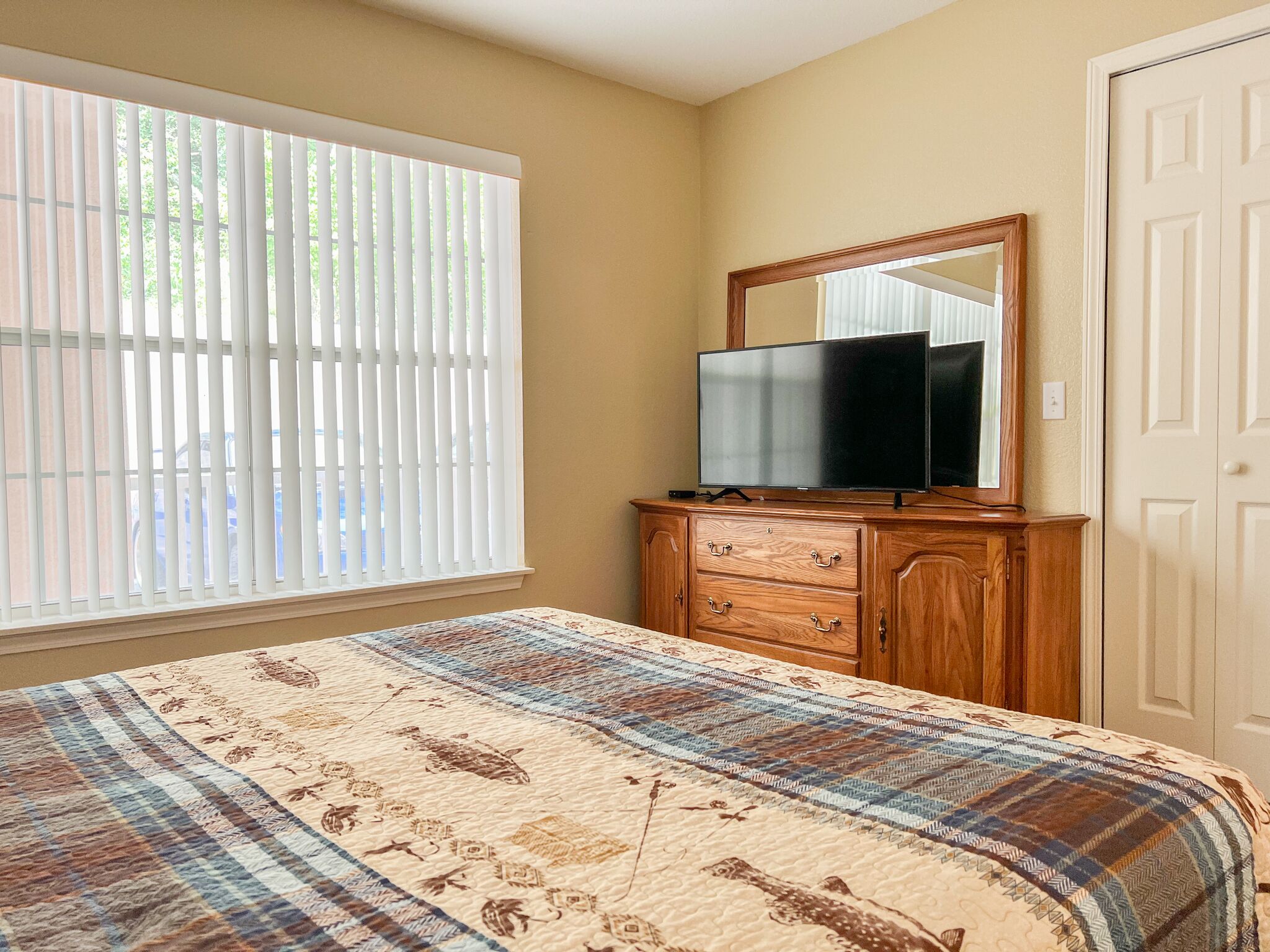 A bedroom with a bed, a dresser, a television, and a window with blinds.