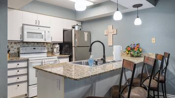 A kitchen with white cabinets, a stainless steel refrigerator, a microwave, and a granite countertop.