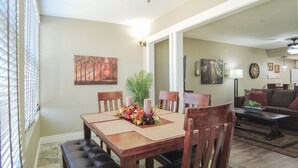 A dining area with a wooden table, four chairs, and a bench. There are two candles and a floral centerpiece on the table.