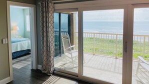 Una habitación con cama, una silla y vista al océano a través de una puerta corrediza de vidrio.