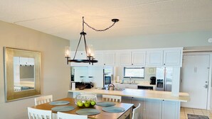 Una cocina moderna con armarios blancos, una isla central y un comedor con mesa de madera y sillas blancas.