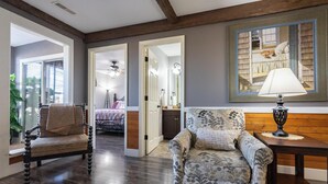 Un salón espacioso con piso de madera, un sillón estampado, una mesita de noche con una lámpara y un cuadro grande enmarcado en la pared.