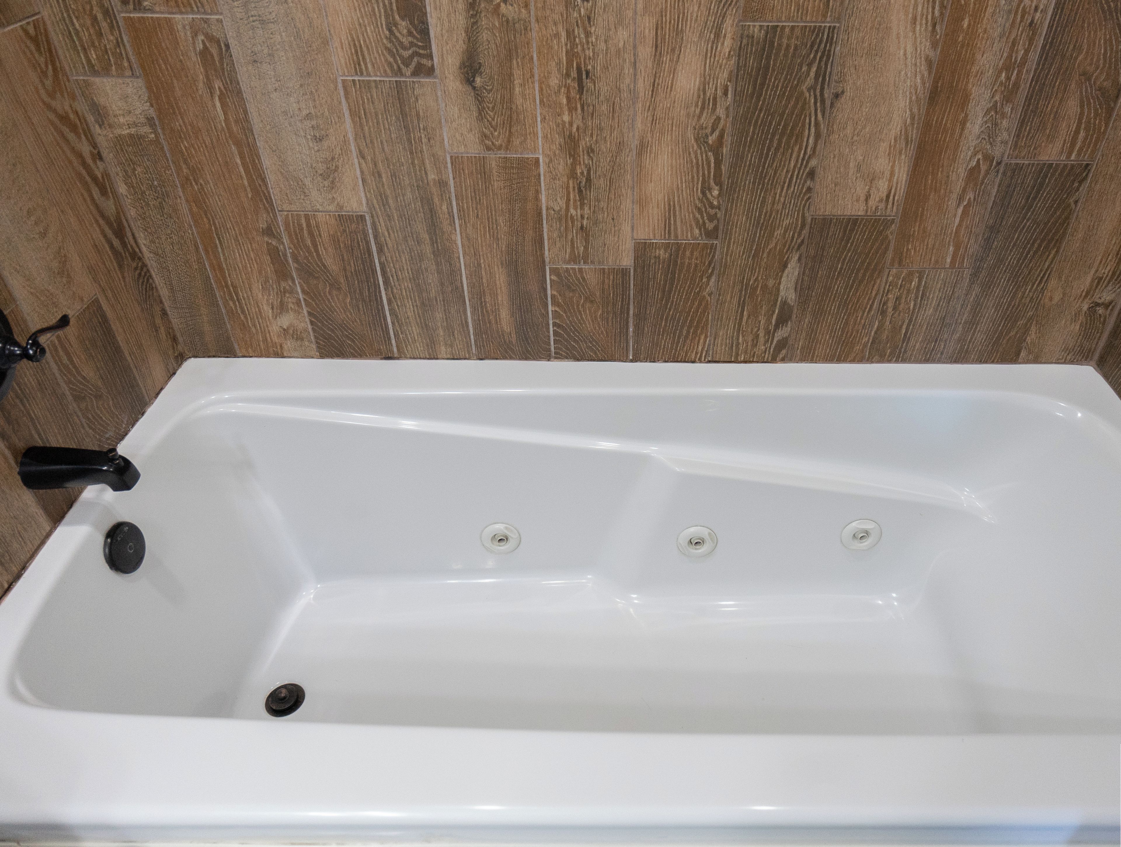 A white bathtub with a black faucet and three drain holes, set against a wooden herringbone-patterned wall.