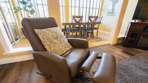 A modern living room with a brown leather sofa, a patterned throw pillow, a dining table with chairs, and a television on a wooden stand. - Walk-In Branson Condo w/ Pool + Easy Access | Club C-7 (Branson)