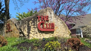 A sign for 'The Club' with a stone backdrop and surrounding greenery. - Walk-In Branson Condo w/ Pool + Easy Access | Club C-7 (Branson)