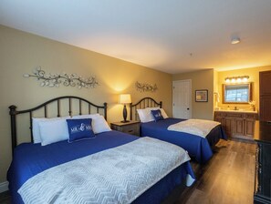 A hotel room with two beds, a kitchenette, and a bathroom.