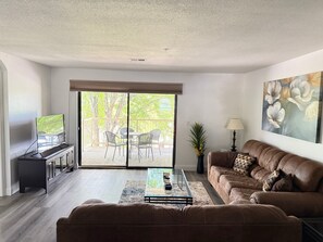 Ein Wohnzimmer mit Sofa, Couchtisch, Fernseher und einer Schiebetür zu einem Außenbereich.