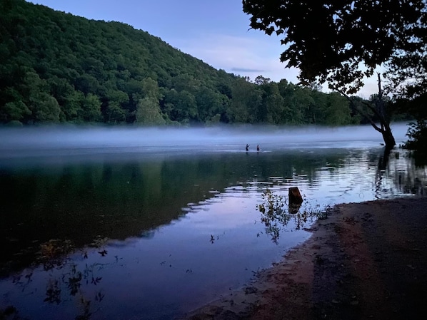 Escape to a serene lakeside haven surrounded by lush greenery and a forested hill.