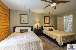 Two single beds with made bedspreads and pillows, a nightstand with a lamp, and a framed floral artwork adorn this cozy space.