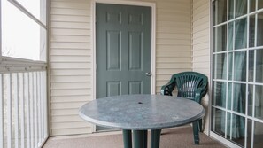 Une table ronde avec une seule chaise, placée sur une véranda dotée d’une porte et d’une fenêtre.