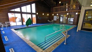Une piscine intérieure avec un fond bleu, un escalier en métal et un balcon en bois.