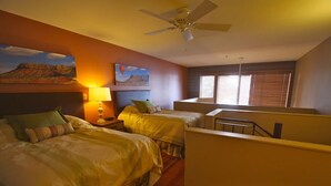 Une chambre d’hôtel avec deux lits, un ventilateur de plafond, un tableau représentant une montagne et une fenêtre avec des stores.