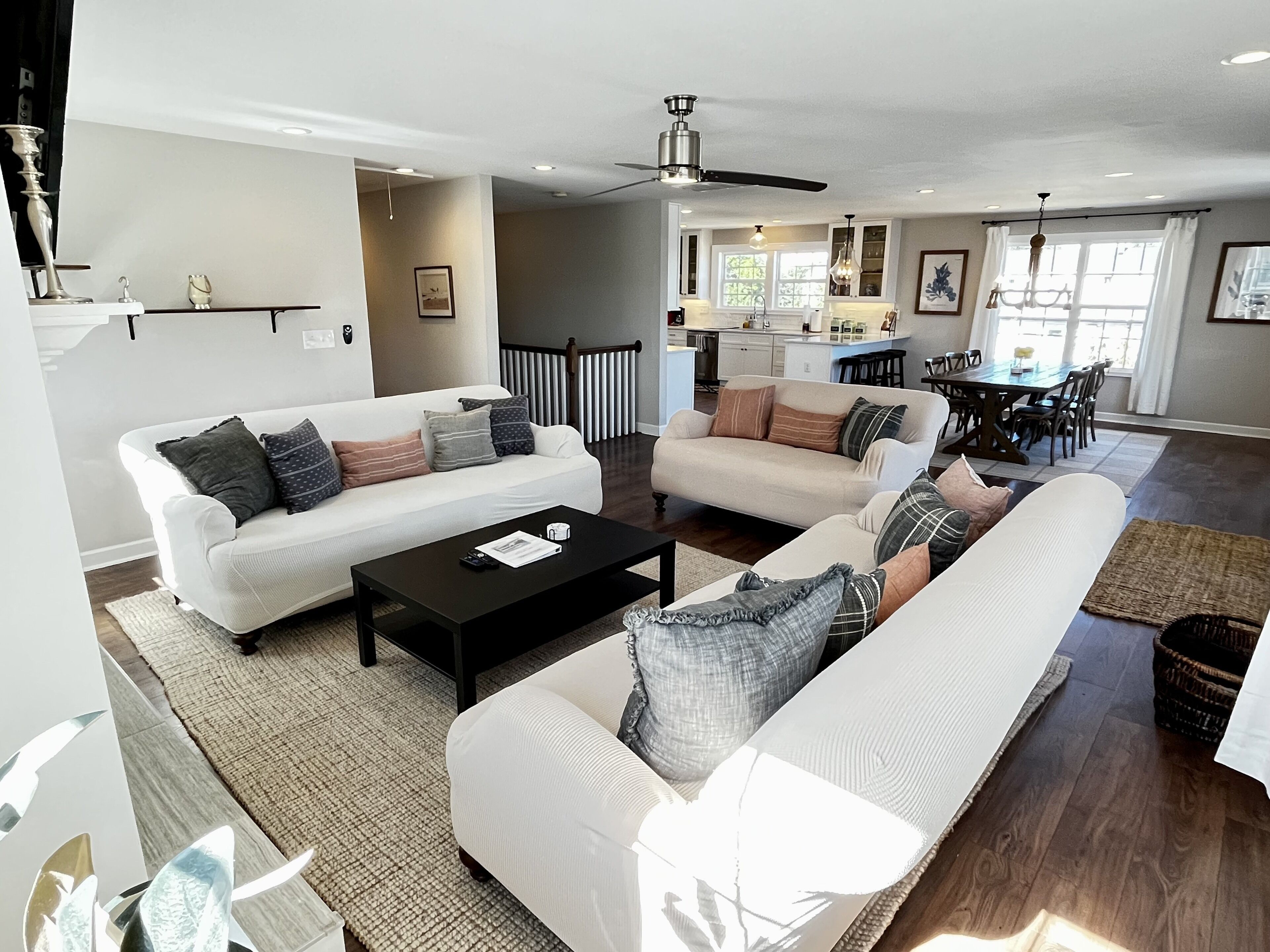 A modern living room with two white sofas, a black coffee table, and a dining area in the background.