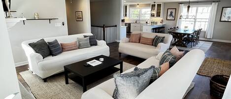 A modern living room with two white sofas, a black coffee table, and a dining area in the background.