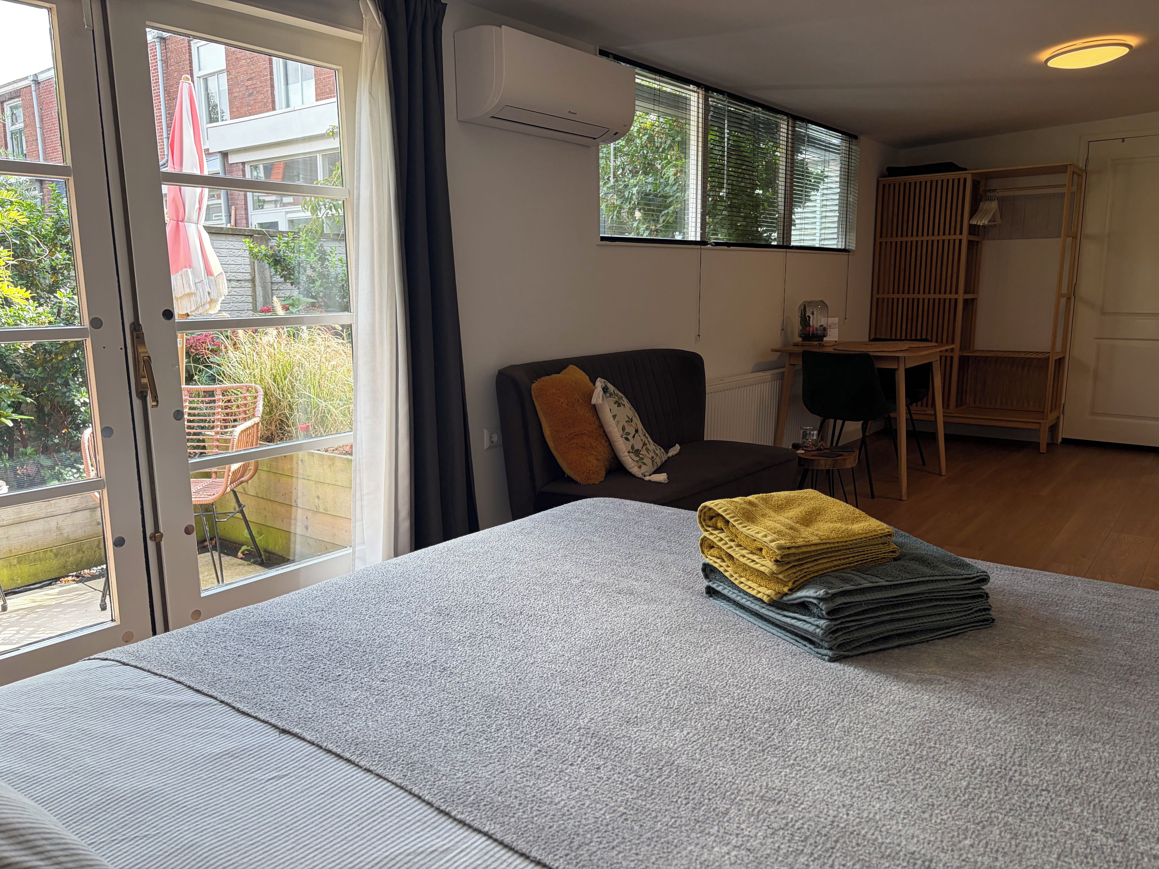 Ein Zimmer mit einem Bett, einem Sessel, einem Tisch und einem fensterbepflanzten Fenster.