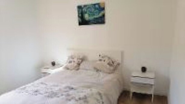 Un dormitorio con cama, mesita de noche y un cuadro colgado en la pared.