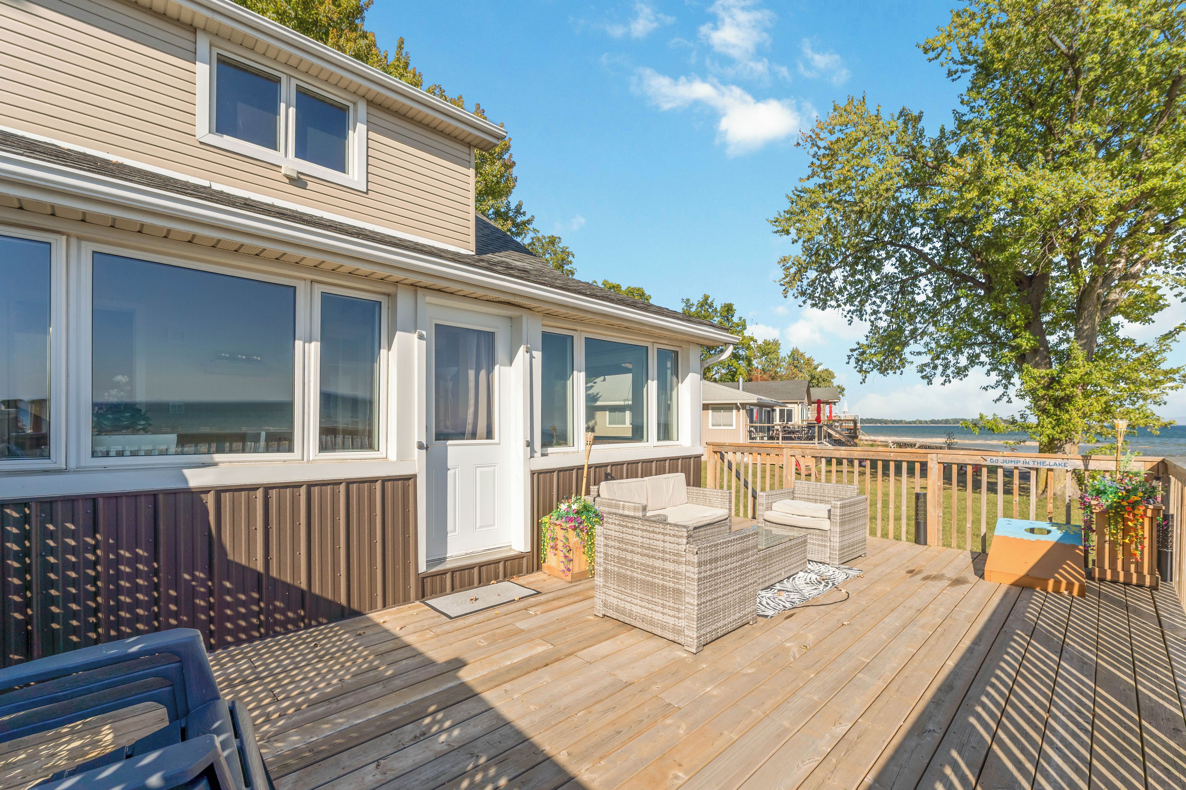 A wooden deck with outdoor furniture, a view of the lake, and a house with large windows.