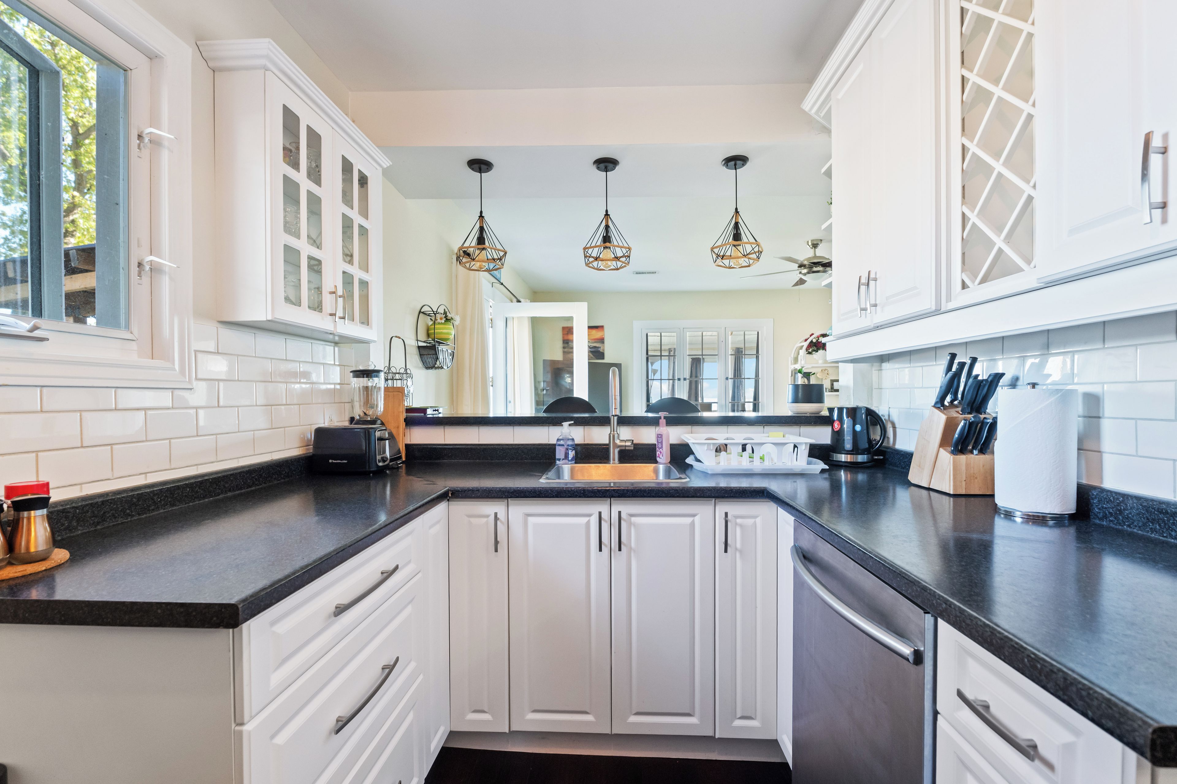 A modern kitchen with white cabinetry, a black countertop, and pendant lighting.