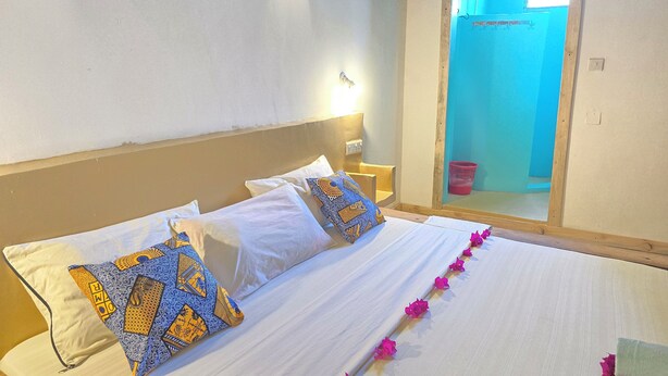 Una cama con sábanas blancas, dos almohadas estampadas y una guirnalda de flores rosadas.