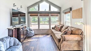 A spacious living room with a high ceiling, large windows, a built-in TV, and a cozy seating area. - Eureka Tiny Home w/ Hot Tub & Community Beach! (Eureka)