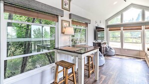 A modern kitchen with large windows, wooden stools, and a dining table. - Eureka Tiny Home w/ Hot Tub & Community Beach! (Eureka)