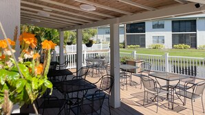 A covered outdoor patio with tables and chairs, a white fence, and a building in the background. - 🌴Palms Heaven Villa•  2BR/2BA/2 Pools & Heated Hot Tubs •Near IMG / Beaches (Bradenton)