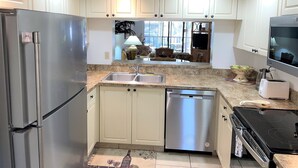 A modern kitchen with stainless steel appliances, white cabinetry, and a large window providing natural light. - 🌴Palms Heaven Villa•  2BR/2BA/2 Pools & Heated Hot Tubs •Near IMG / Beaches (Bradenton)