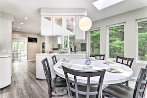 Una cocina moderna con una isla central, armarios blancos y un comedor con una mesa redonda y sillas.
