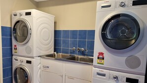 A compact laundry room with stacked Bosch and Clark washing machines, a sink, and blue tiled walls. - Blue Wren Lodge Waratah (Waratah West)