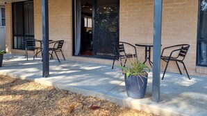 An outdoor patio with brick walls, metal chairs, and a potted plant. - Blue Wren Lodge Waratah (Waratah West)