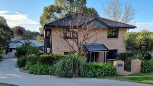 A two-story house with a brick exterior, a tiled roof, and a front yard with various plants and a mailbox. - Blue Wren Lodge Waratah (Waratah West)