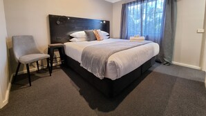 A hotel room with a large bed, a chair, a nightstand, and a window with curtains. - Blue Wren Lodge Waratah (Waratah West)