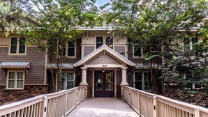 Une passerelle en bois mène à un bâtiment doté d’une façade en pierre et de nombreuses fenêtres.