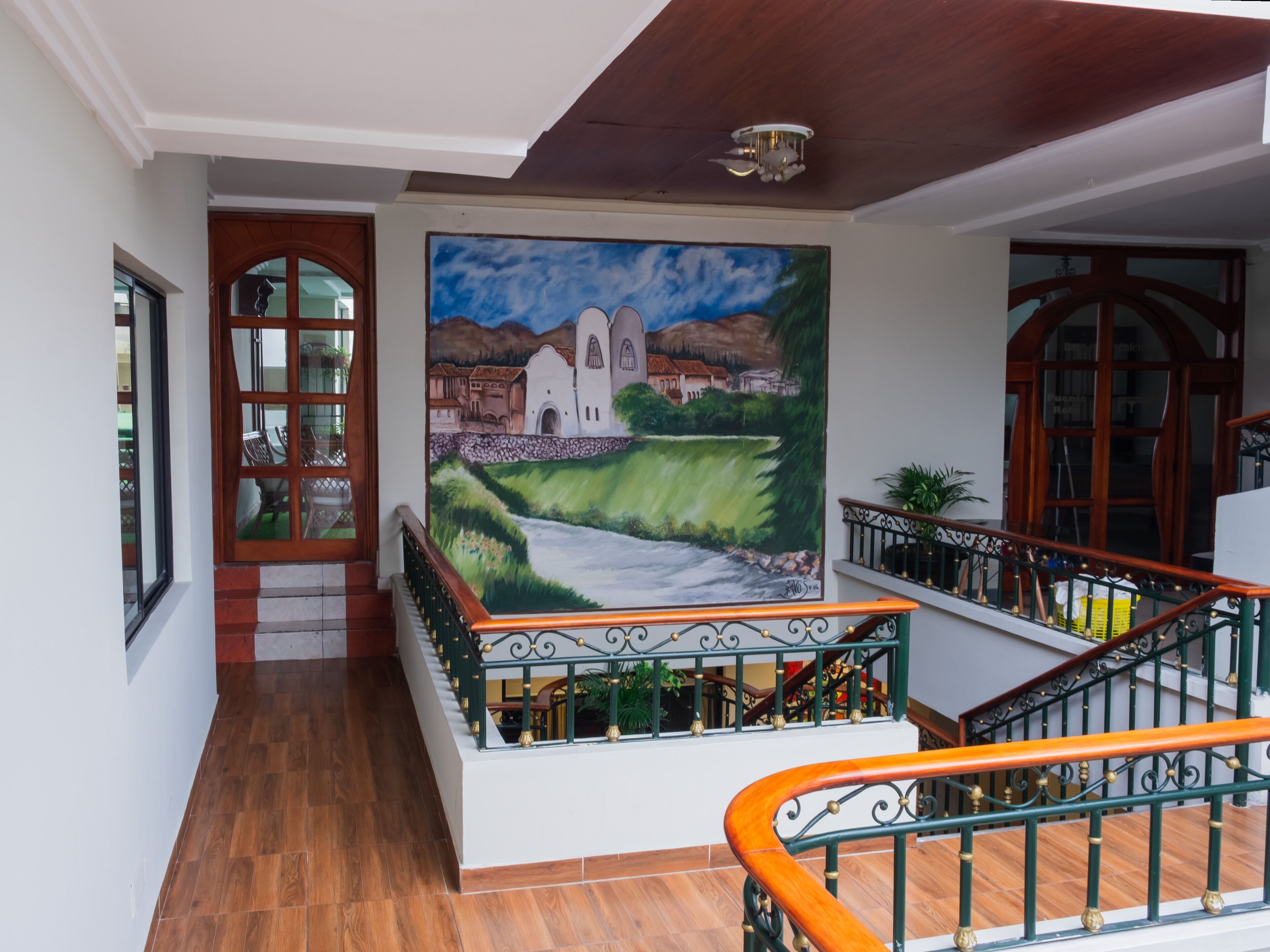A staircase with a wooden handrail and green balusters, leading to a landing with a mural of a landscape.