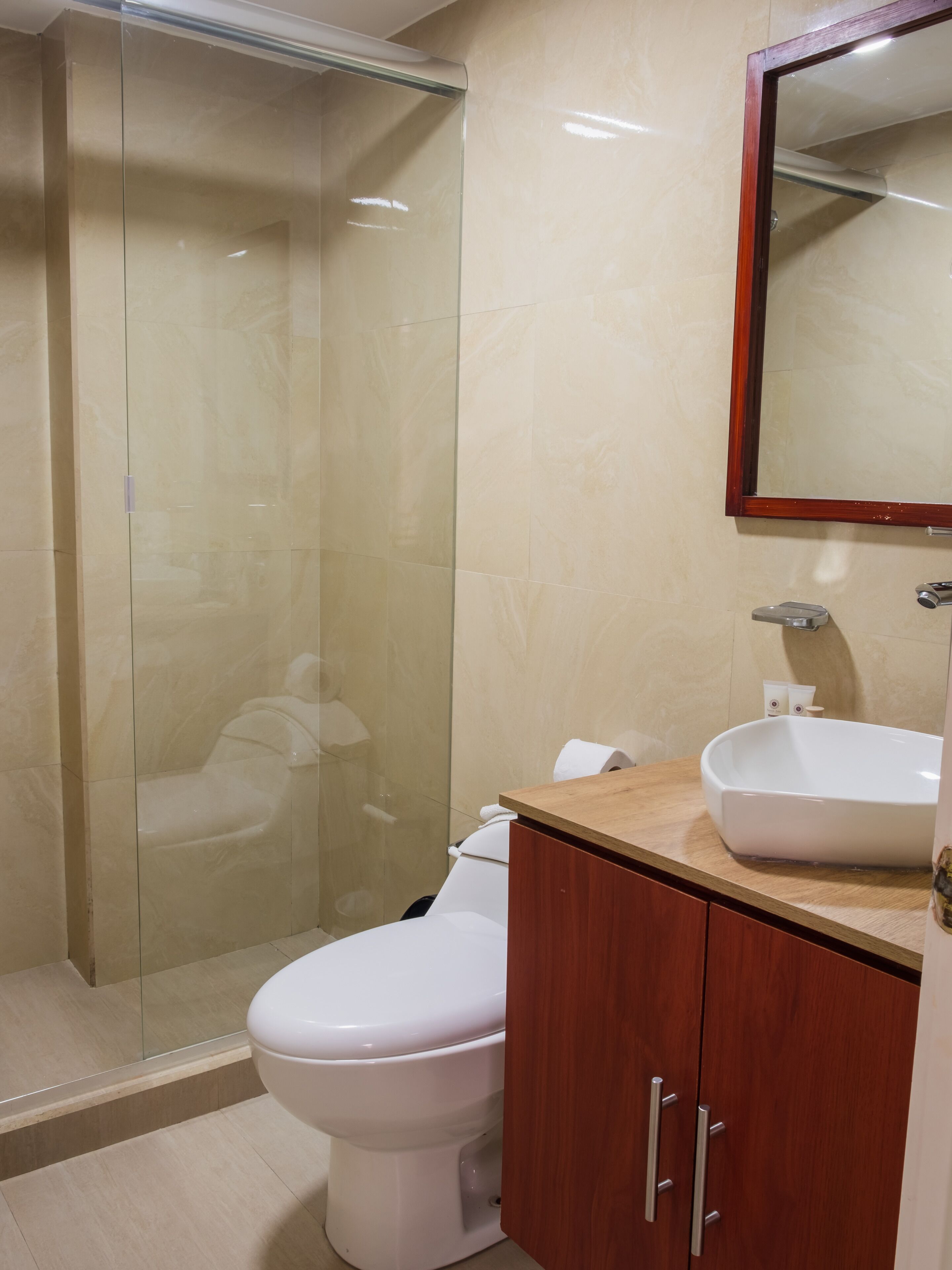 A bathroom with a glass shower enclosure, a white toilet, a wooden vanity with a sink, and a mirror above the sink.