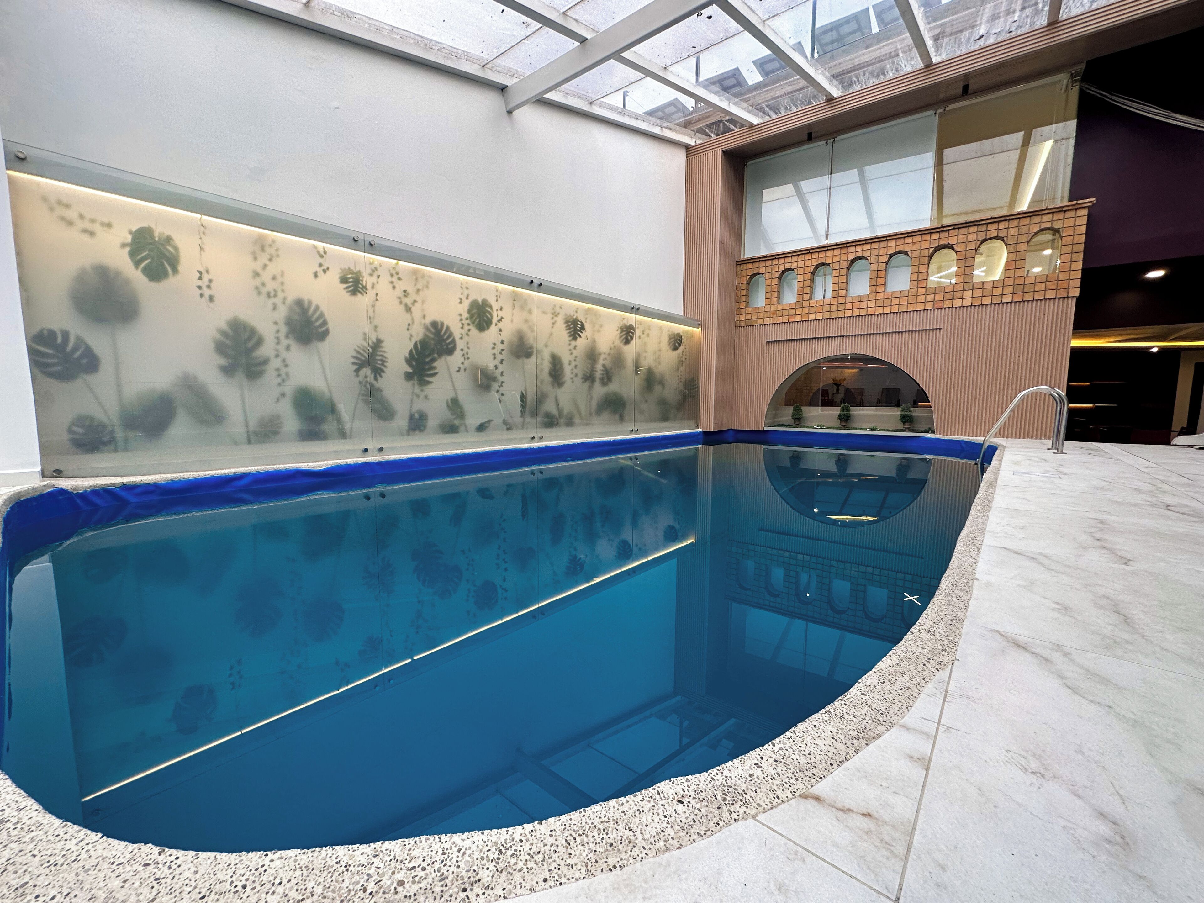 Ein Innenpool mit klarem, blauem Wasser, umgeben von einem Kiesstreifen und einer Wand mit Blattmotiven.