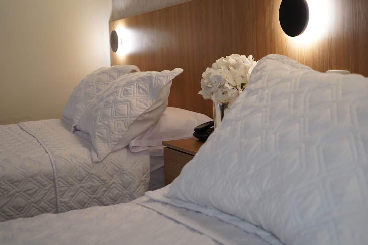 Ein Hotelzimmer mit zwei Betten, einem Nachttisch und einer Blumenvase.