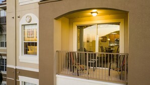 A balcony with a railing, a dining area with chairs and a table, and a kitchen visible through the glass doors. - Location,Location,Orlando3bdr 2bthl,Resort near all parks, Conv.Ctr, Int. Dr (Orlando)