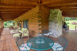 A log cabin with a covered porch, outdoor seating, and a stone wall.