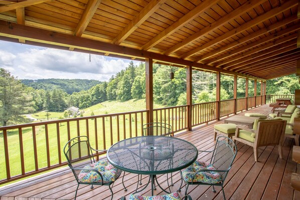A covered outdoor deck with a table and chairs, overlooking a lush green landscape.