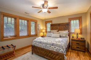 A bedroom with a wooden bed, a ceiling fan, and large windows with blinds.