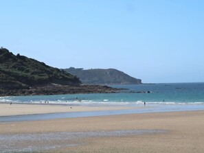 A beach with a rocky cliff and calm sea.