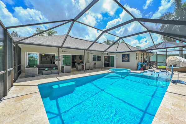 Ein Schwimmbecken mit überdachtem Patio, Gartenmöbeln und blauem Himmel.